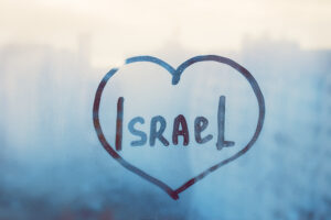 Handgeschriebenes Wort Israel in Herzform auf beschlagenem blauen Fenster mit Regentropfen